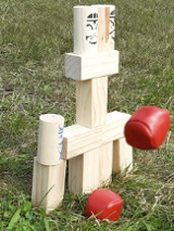 Wieża z klocków na trawie i lecąca w jej kierunku mała piłeczka.