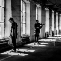 Czarno-biała fotografia złożona z kilku nałożonych na siebie kadrów. Kadry te przedstawiają dwóch mężczyzn z instrumentami. Muzycy są ujęci w różnych pozach, jeden z mężczyzn gra na skrzypcach.