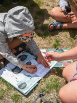 Dziecko z mamą siedzą na trawie pochyleni nad broszurką.