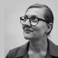 Na zdjęciu jest Marta Madejska, w portretowym ujęciu. Ma związane, gładko zaczesane włosy, okulary w wyrazistych oprawkach i marynarkę. Jej głowa skierowana jest w lewo, patrzy w górę z delikatnym uśmiechem.