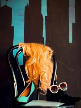 Na czarnym krześle stoi czarny męski but, na nim leżą różowe okulary, obok stoi damki zielony but na wysokim obcasie. Na oparciu krzesła wisi peruka z długimi blond włosami.