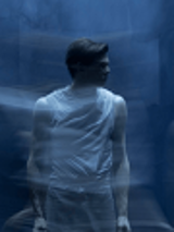 Zdjęcie stojącego mężczyzny, który patrzy w bok. Niebieskie, rozmyte tło.