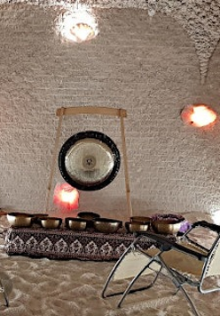 W grocie ściany z cegły na podłodze: misy i gong na stojaku a drugi oparty o ścianę. Z przodu 2 leżaki.