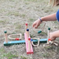 Gra dla dzieci. Drewniane kolumienki, na które dzieci rzucają pętle ze sznurka.