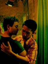 Dwóch mężczyzn tańczących razem pod oknem w mieszkaniu. Za oknem plac budowy.