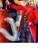 zdjęcie przedstawia postać w kolorowym stroju stojącą przy machinie przypominjącej rakietę