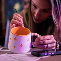 Kobieta maluje kubek ceramiczny.