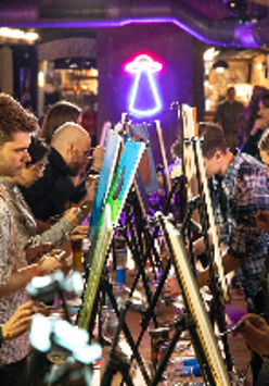 Grupa osób stoi przed sztalugami i maluje obrazy.