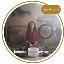 Kobieta w średnim wieku z czarnymi włosami. Ubrana w czerwony długi rękaw i wzorzyste spodnie. Siedzi na podłodze. Za nią wiszą 2 gongi. Przed nią leży kilka mis.