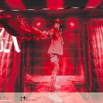 Obrazek informje o spektaklu Nasza racja. Widać na nim postać na scenie, oświetloną czerwonymi światłami.