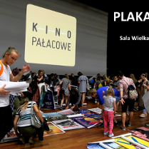 Ludzie poszukujący plakatów rozłożonych na ziemi. W tle ekran z wyświetlonym złotym logo "Kino pałacowe".