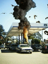 Obrazek przedstawia sztuczne wyuchy na stacji benzynowej położonej na obrzeżach miasta. Dookoła latają ptaki. Wybuchy i ptaki wyglądają jakby były zrobione w paint-cie.