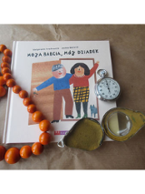 Okładka książki "Moja Babcia, mój Dziadek" obok korale i zegarek.