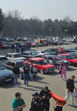 Parking, na którym spacerują ludzie między licznymi klasycznymi samochodami.