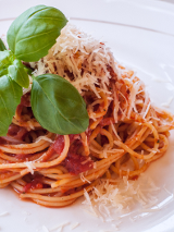 Zdjęcie makaronu z sosem pomidorowym udekorowany listkmi bazylii.