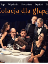 Przy stole siedzą dwaj mężczyźni i dwie kobiety. Za nimi stoi dwóch mężczyzn, wszyscy ubrani galowo.