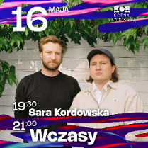 dwójka wykonawców na tle nialej sciany budynku i zwisajacych zielonych lisci