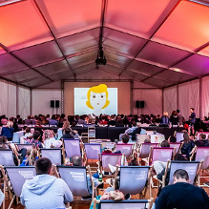 Ludzie siedzący na lrżakach i oglądający film w plenerze, pod namiotem.