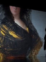 Kobieta stojąca przed wyświetlającym się na ścianie z rzutnika popiersiem elegancko ubranej kobiety.