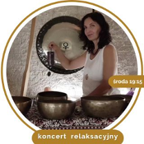 Kobieta w średnim wieku, w białej koszule, z czarnymi kręconymi włosami. Stoi przy rozłozonych złotych misach.