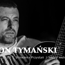 Czarno-białe, bliskie ujęcie mężczyzny z krótkim zarostem, który patrzy w bok z lekkim uśmiechem. W dolnej części kadru widoczny jest gryf i fragment korpusu gitary akustycznej trzymanej przez artystę. Tło jest ciemne i nieostre. Na froncie napisy, będące szczegółami wydarzenia, które są zawarte w artykule.