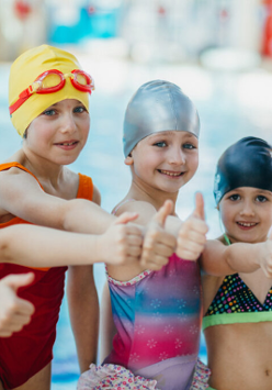 Grupa dzieci w strojach pływackich i czepkach stoi na basenie.