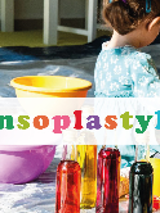 Napis sensoplastyka, za nim dziecko stojące wśród misek.