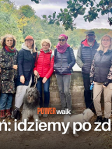 Grupa ludzi stoi przy murku obok jeziora Rusałka. Przed nimi napis o treści Poznań idziemy po zdrowie.