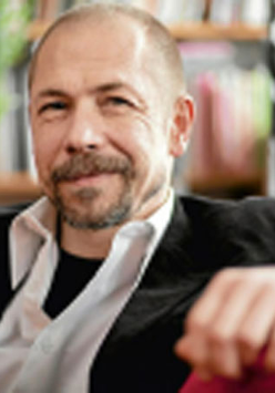 Profesor siedzi na kanapie, na tle regaów z książkami.
