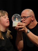 2 aktorów z niepełnosprawnosciami. Męszczyzna trzyma kulę z ośnieżonym drzewkiem.