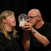 2 aktorów z niepełnosprawnosciami. Męszczyzna trzyma kulę z ośnieżonym drzewkiem.