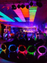 Zdjęcie przedstawia widok z imprezy klubowej. Znajduje się na nim wiele osób i intensywnych świateł, rozświetlających półmrok panujący w pomieszczeniu.