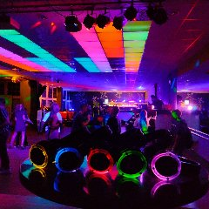 Zdjęcie przedstawia widok z imprezy klubowej. Znajduje się na nim wiele osób i intensywnych świateł, rozświetlających półmrok panujący w pomieszczeniu.