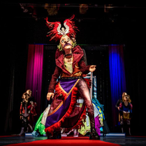 Zdjęcie ze spekatklu - na pierwszym planie aktor w stroju i masce, na drugim planie czterech aktorów.