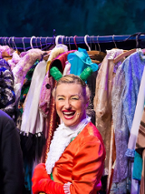 Zdjęcie ze spektaklu - aktorka w przebraniu do przedstawienia na tle wieszaka pełnego ubrań.