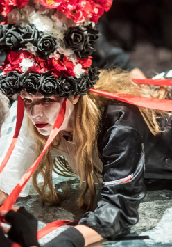 Zdjęcie ze spektaklu - kobieta z czepcem w biało-czerwono-białych kolorach na głowie, leżąca i patrzaca na mężczyznę, którego twarz jest niewidoczna.