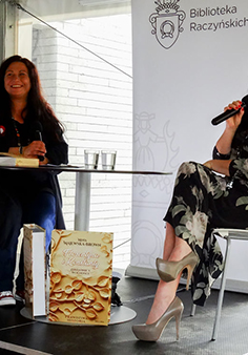 Dwie kobiety siedzące na krzesłach w Bibliotece Raczyńskich. Jedna z nich trzyma w ręce mikrofon.