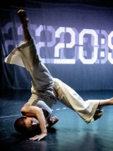 Zdjęcie przedstawia tancerkę znajdujacą się na scenie. W jej tle wyświetlany jest zegar.