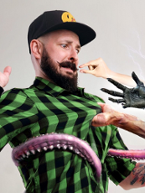 Plakat zapowiada nowy program stand-up Adama Van Bendlera zatytułowany "Ultimatum". Artysta w zielonej koszuli w kratę i czapce z daszkiem jest wciągany przez smartfona, z którego wyrastają macki i demoniczne dłonie. Kompozycja utrzymana jest w jasnej kolorystyce z wyraźnymi napisami w kolorach pomarańczowym i zielonym.