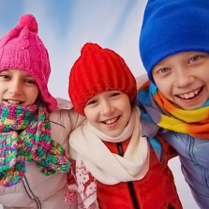 Dziewczynka i dwóch chłopców ubrani w czapki i szale usmiechają się obejmujmą.