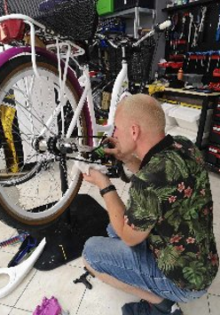 Mężczyna siedzi przed rowerem i majsterkuje przy nim.