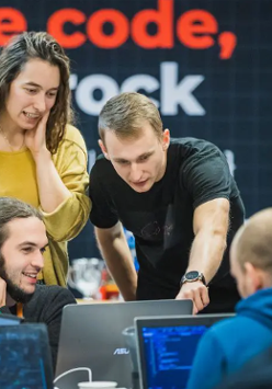 Dwóch mężczyzn i kobieta stoją przy stanowisku komputerowym. Rozmawiają na temat tego, co widzą na ekranie.