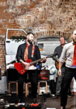 Na zdjęciu czteroosobowy zespół muzyczny na tle muru.