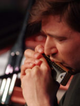 Zdjęcie twarzy mężczyzny grającego na harmonijce.