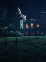 Kadr z filmu "Gniazdo zła" przedstawia gotycką posiadłość, stojącą na pagórku. Na zboczu pagórka krzyże. Jest ciemno i mroczno.