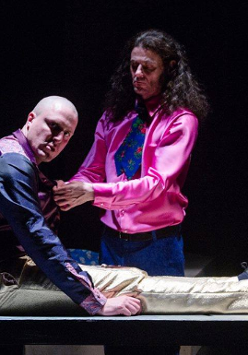 Na zdjęciu dwóch aktorów na czarnym tle. Jeden siedzi z wyprostowanymi nogami, drugi klęczy obok.