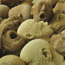 Fotografia z wystawy Andrzeja Okińczyca "W Imię Boga Jedynego" przedstawia liczne rozrzucone, chaotycznie kamienne głowy z twarzami zastygłymi w krzyku.