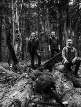 Na czarno-białym zdjęciu trzy postaci mężczyzn w lesie.