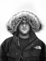 Na zdjęciu młody mężczyzna w zimowej kurtce z założonym na głowę kapturem.