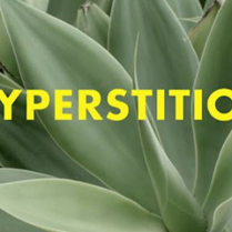 Żółty napis "hiperstition" na tle zielonych liści aloesu